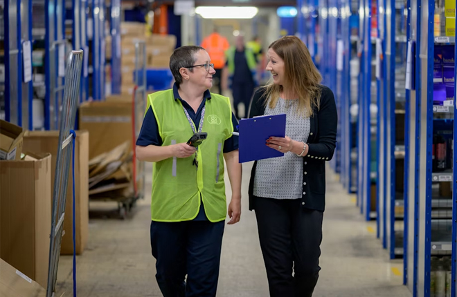 Two women walking through a warehouse and talking.