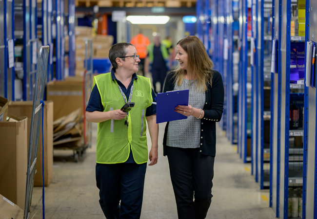 Two women walking through a warehouse and talking.
